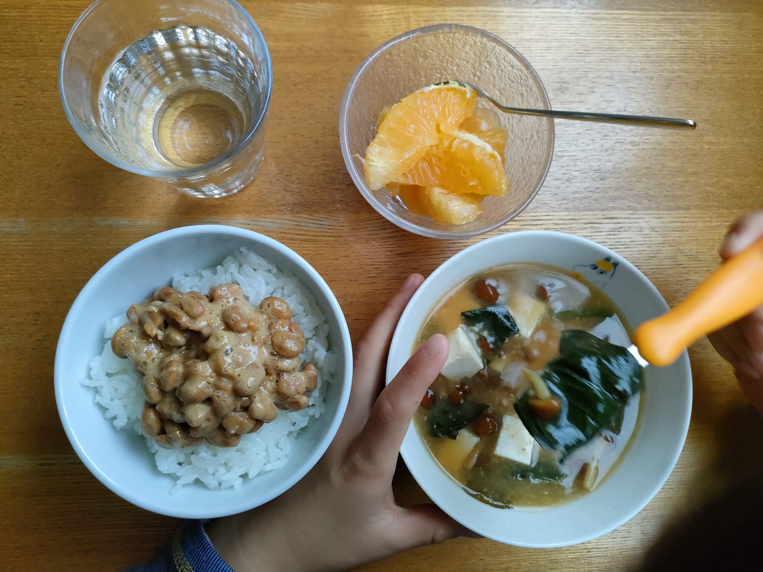 豆ご飯と味噌汁、果物のある朝食で味噌汁を食べようとする子どもの様子