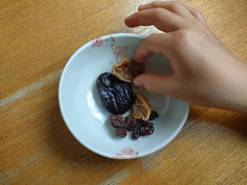 皿に盛ったいちじく、プルーン、レーズンを子どもが手で取ろうとしている様子