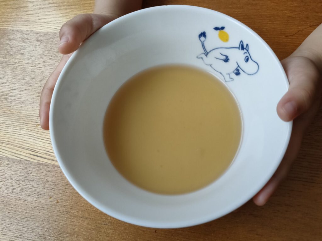 子どもが味噌汁の上澄みが入ったお椀を両手で持っている