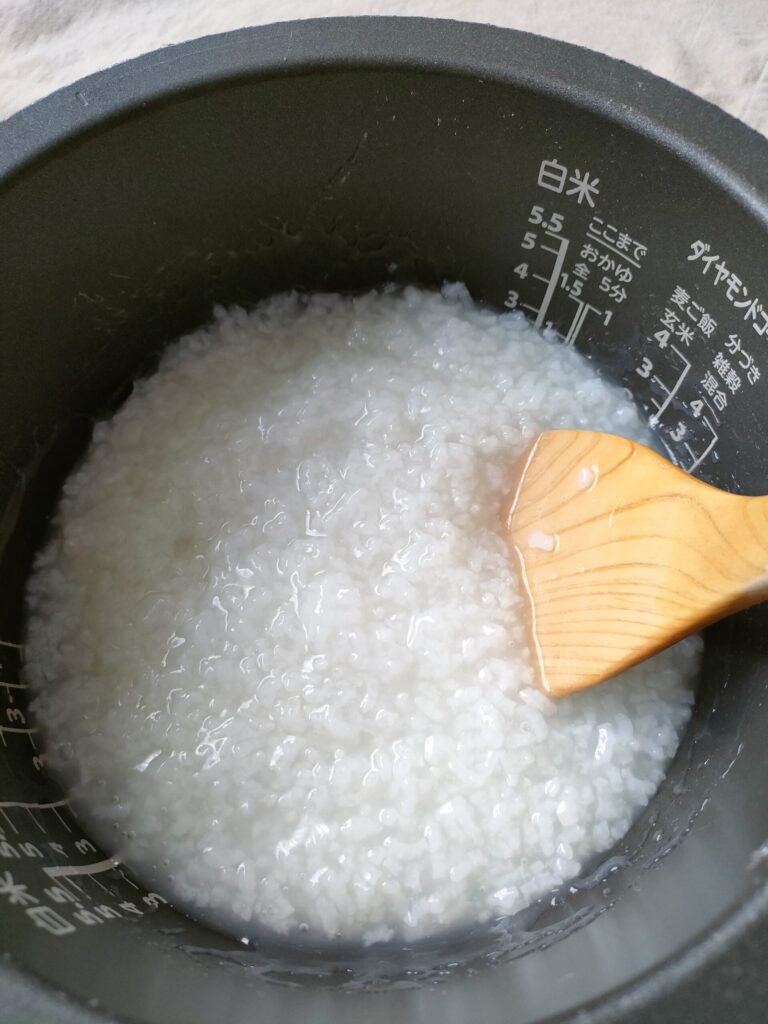 炊飯器で炊き上がったお粥を木のしゃもじで混ぜている様子