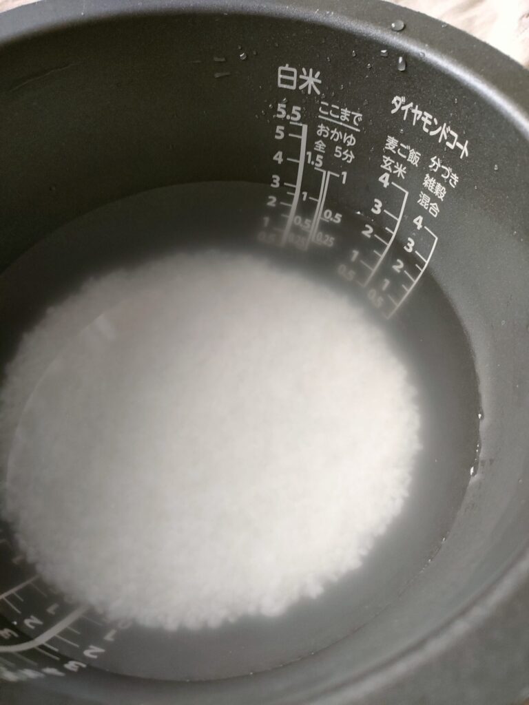 炊飯器のお釜に洗った米を入れ、お粥用の水加減をしている様子