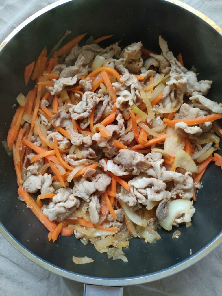 豚肉と玉ねぎ、人参をフライパンで炒めて火を通している様子