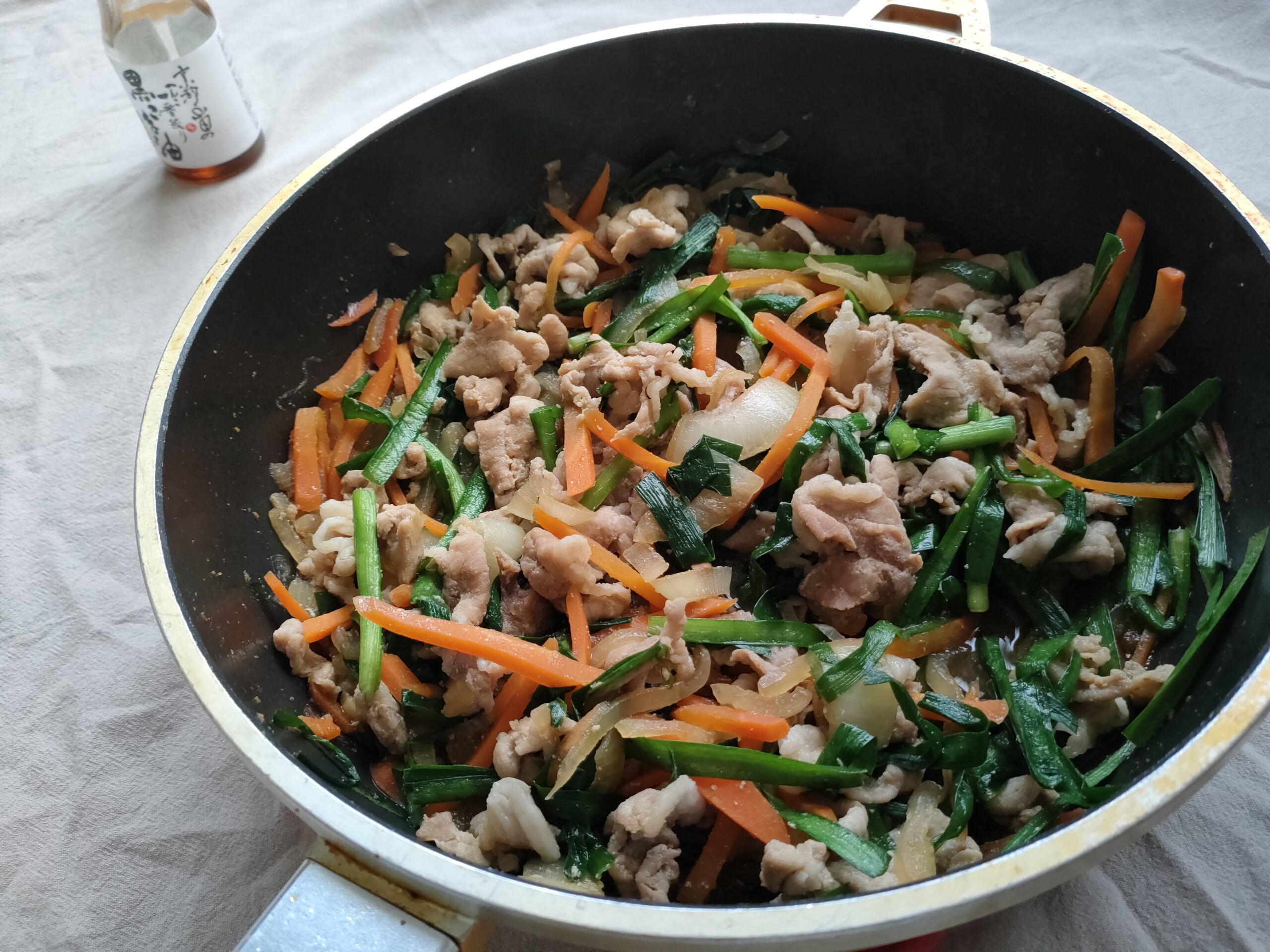 フライパンの中で豚肉と野菜を使ったプルコギ丼が完成し、奥にごま油の瓶が写っている様子
