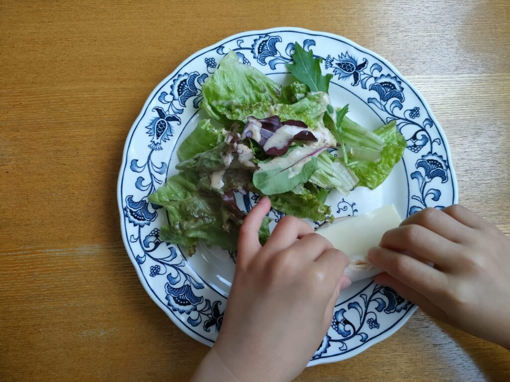子どもの手でハムとスライスチーズを巻いている様子
