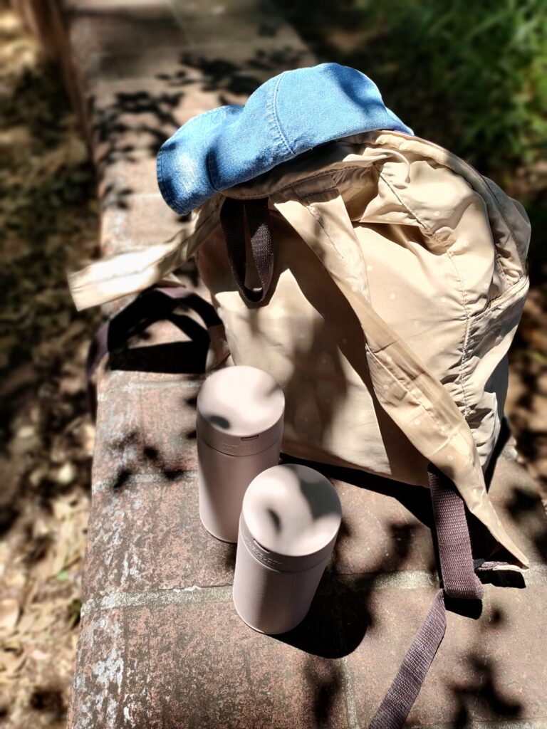 公園のレンガのベンチに置いたリュックと帽子、水筒に木漏れ日が当たっている様子